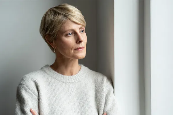 Fatigue-and-Low-Energy-Clinic A blond, middle-aged woman looks out the window with a tired expression. Schedule fatigue and low energy treatment from Tasmin Cordie, D.C. of Sage Functional Medicine in Marlboro Township.