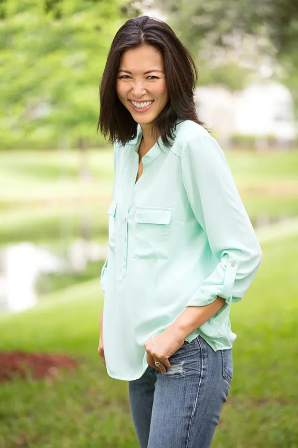 A middle-aged brunette woman in a light green button-up shirt stands outside smiling, happy with her perimenopause treatment from Tasmin Cordie, D.C. of Sage Functional Medicine in Marlboro Township.