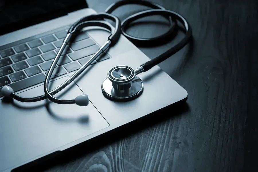 An open laptop with a stethoscope lying on it on a wooden table, symbolizing telemedicine care from Tasmin Cordie, D.C. of Sage Functional Medicine in Marlboro Township.