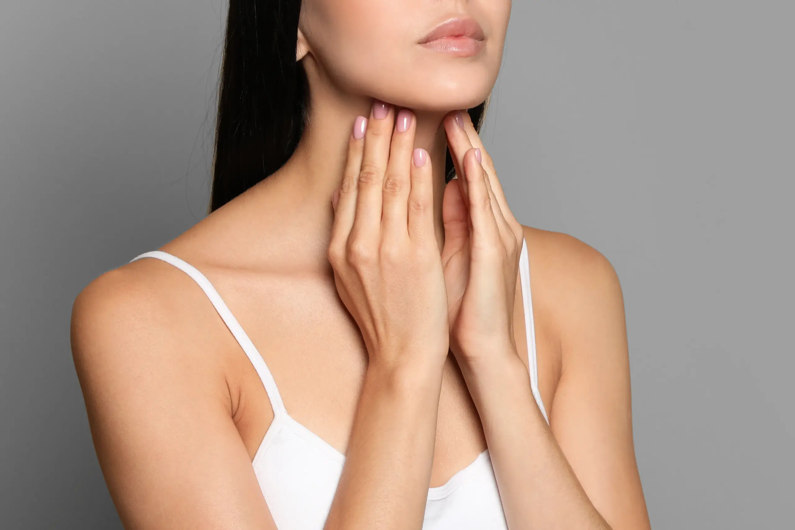 A woman in a white tank top touches her neck looking for signs of thyroid disorder. Get help for thyroid disorders from Tasmin Cordie, D.C. of Sage Functional Medicine in Marlboro Township.