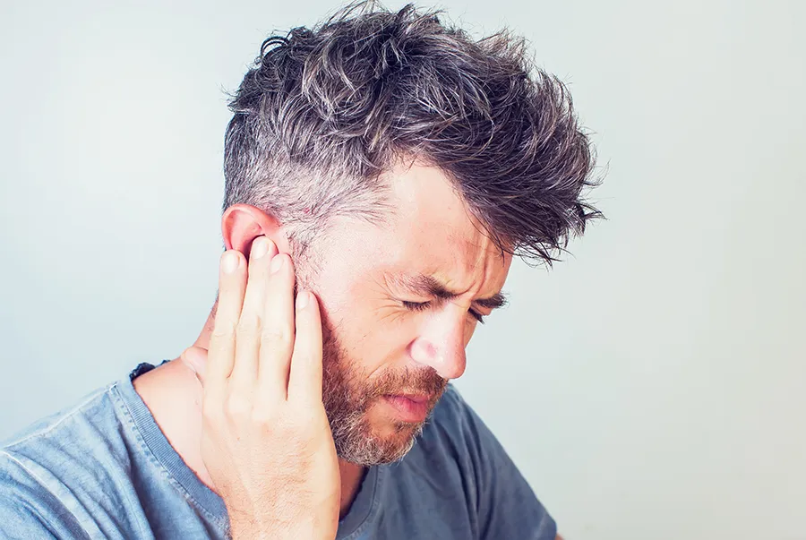 A man with tinnitus holds his ear in discomfort. Get treatment for tinnitus from Tasmin Cordie, D.C. of Sage Functional Medicine in Marlboro Township.