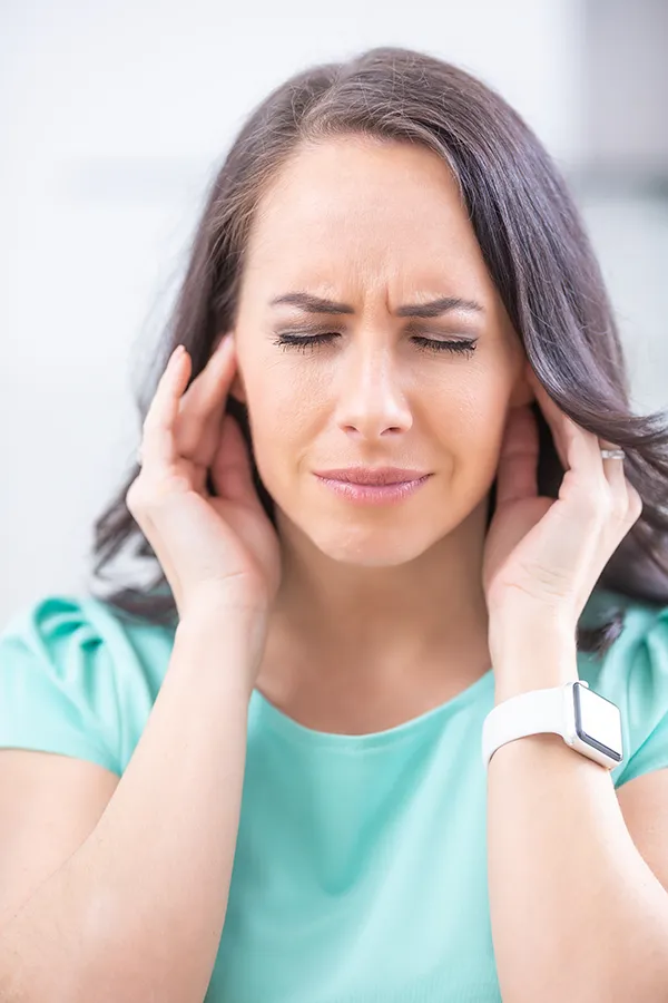 A woman with tinnitus holds her ears in discomfort. Get treatment for tinnitus from Tasmin Cordie, D.C. of Sage Functional Medicine in Marlboro Township.