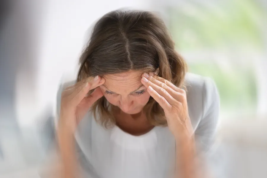A woman with a spinning sensations holds her forehead. Get treatment for vertigo and balance issues from Tasmin Cordie, D.C. of Sage Functional Medicine in Marlboro Township.