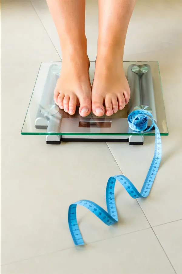 Close-up of a woman's feet standing on a scale, with measuring tape by her toes, getting treatment for weight loss resistance from Tasmin Cordie, D.C. of Sage Functional Medicine in Marlboro Township.